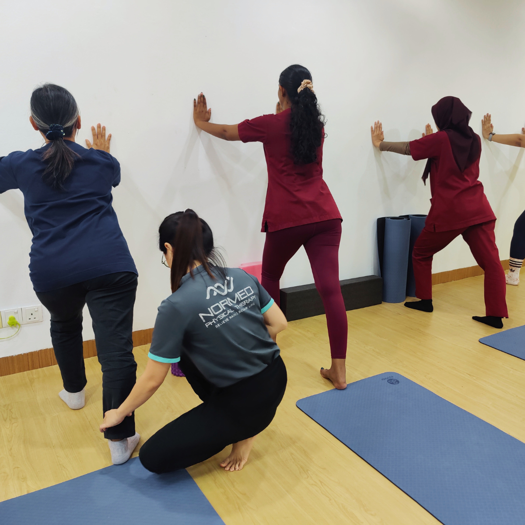 A diverse group of individuals struggle with yoga and pilates seated on mats in a spacious room doing stretching and strengthening exercises